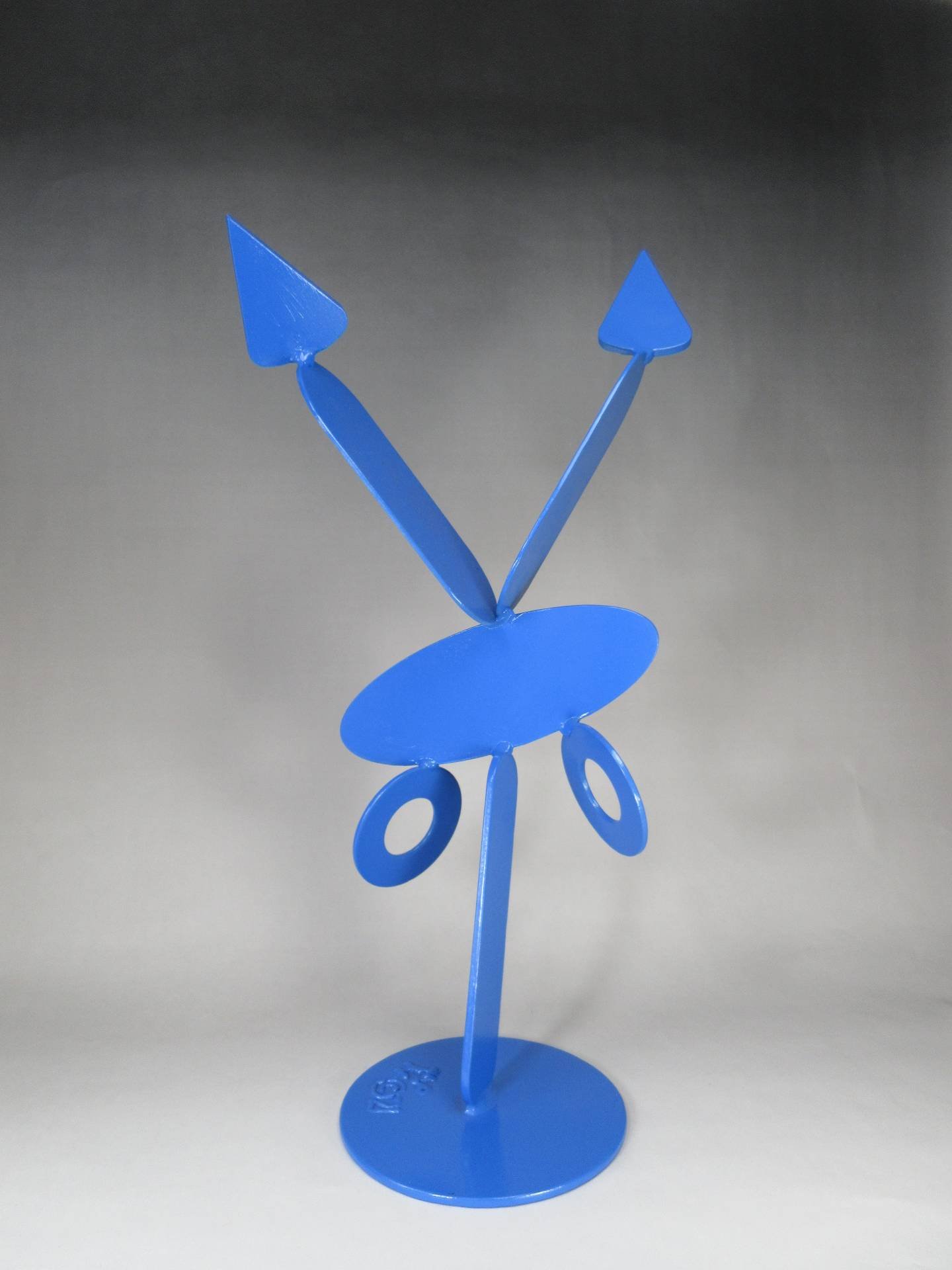Blue metal sculpture with a vertical base and two upward angled arms ending in triangular shapes, with circular elements below a central disc. By Michael Herold.