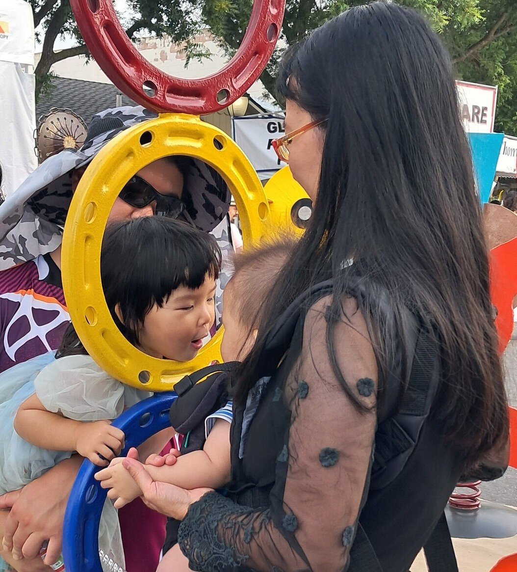 Family interacting with Michael Herold public sculpture at an outdoor art festival, capturing a shared moment of curiosity, connection, and community engagement.