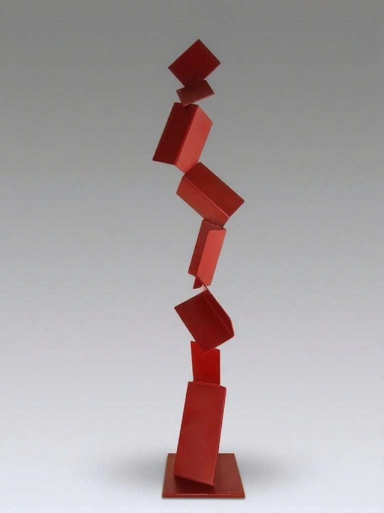 Red metal sculpture composed of stacked, angled rectangular forms rising vertically on a base, creating a dynamic, figure-like structure. By Michael Herold.