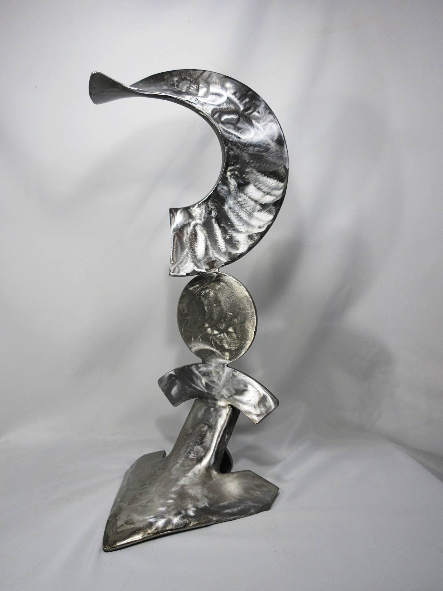 Metal sculpture featuring a curved crescent-like form above a circular element and angled base, creating a vertical, symbolic composition. By Michael Herold.