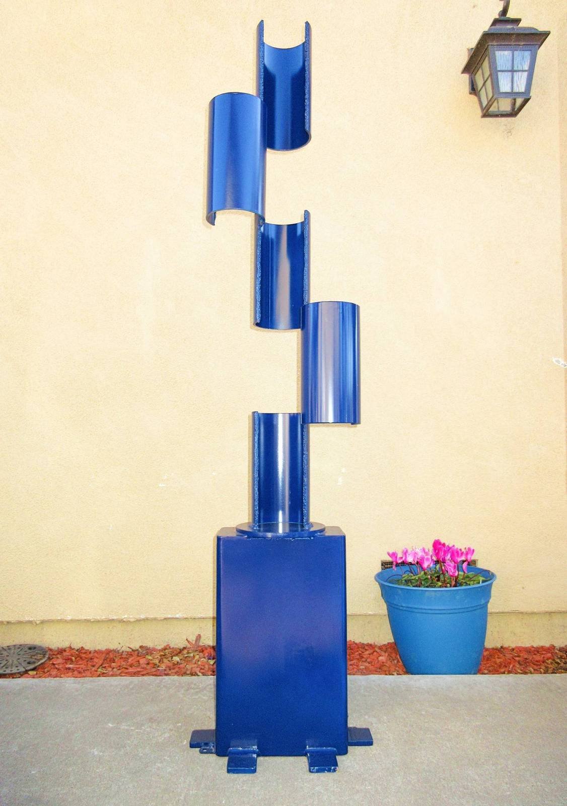Blue metal sculpture composed of stacked curved cylindrical sections arranged vertically on a rectangular base.